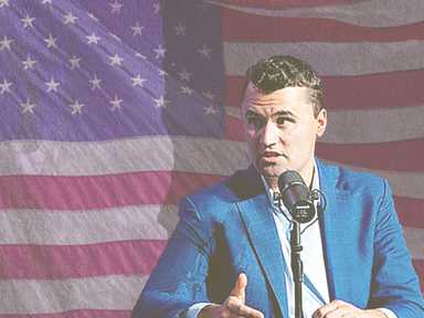 Charlie Kirk sitzt vor einer amerikanischen Flagge.