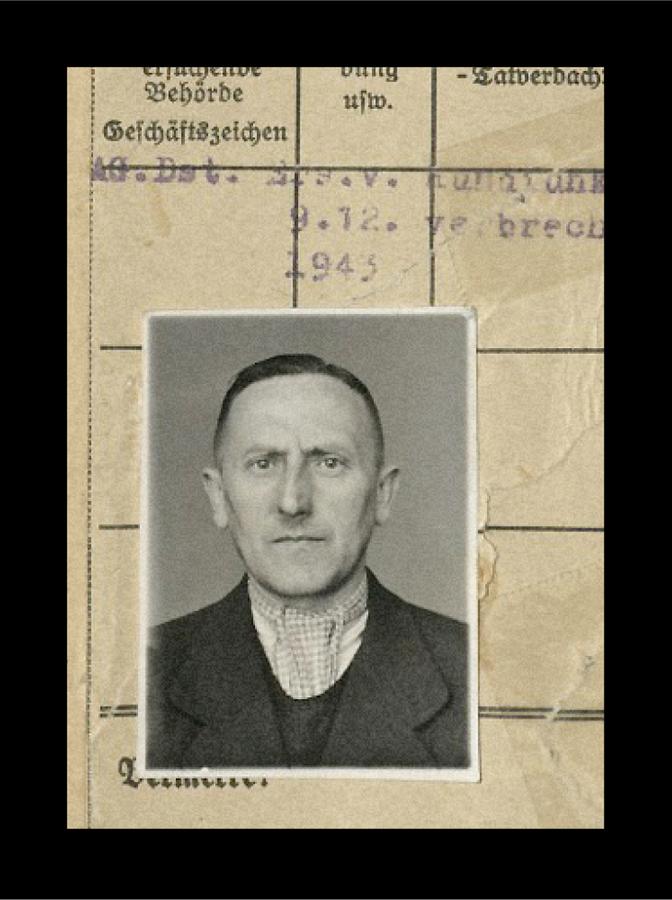 Schwarz-Weiß-Porträt eines Mannes mit kurzen Haaren, der einen Anzug und ein kariertes Hemd trägt, vor einem Hintergrund mit alten Dokumenten.