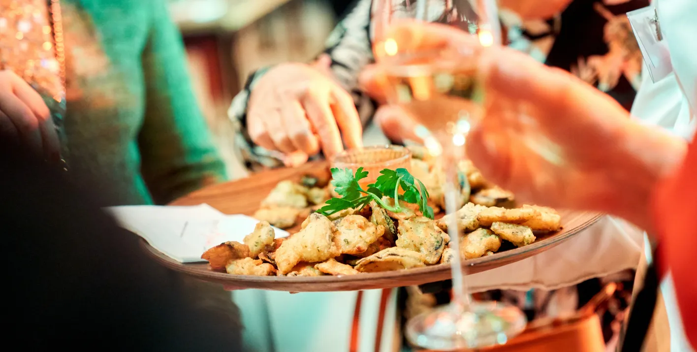 hands taking a food from the waiter with a champagne glass in the other hand