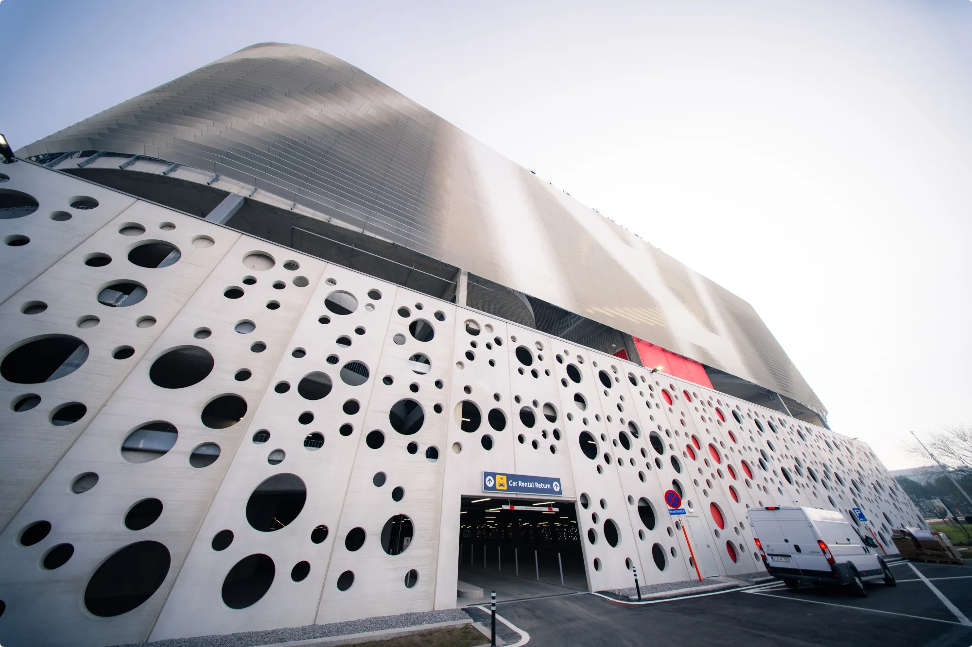 Modern building facade with perforated white panels, black circular patterns, and a large overhang, viewed from a low angle.