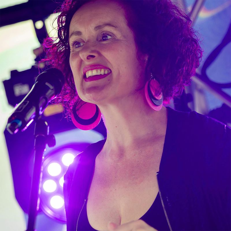 A photography of a person with curly hair singing into a microphone wearing round pink earrings.