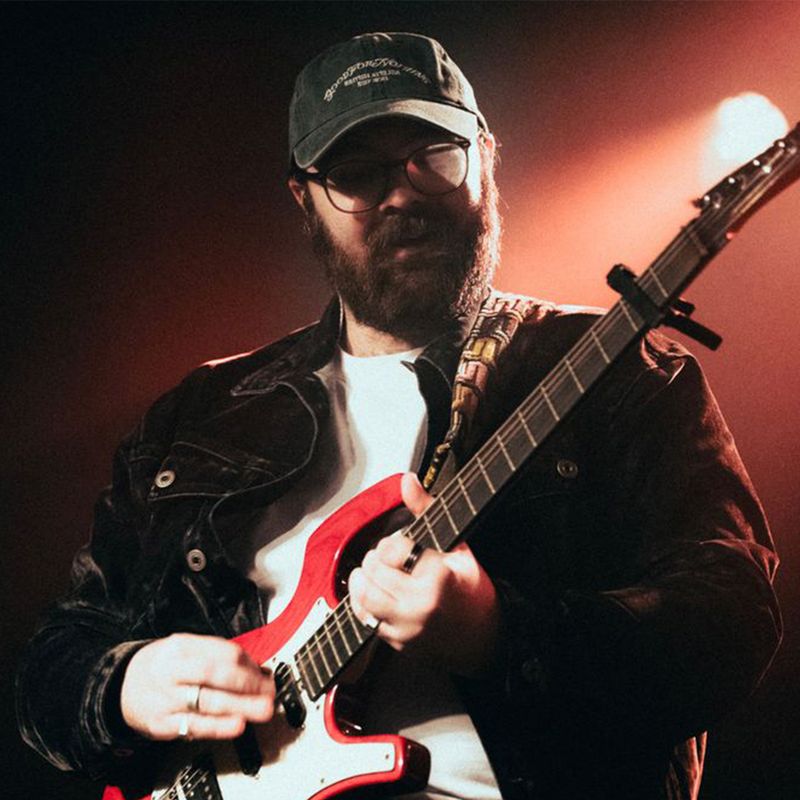 A man in a cap and glasses playing electric guitar on stage