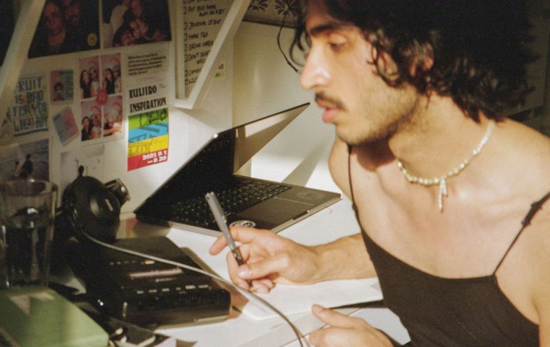 Photograph of Hamza Ashraf sat at a workspace holding a pen whilst looking forward.