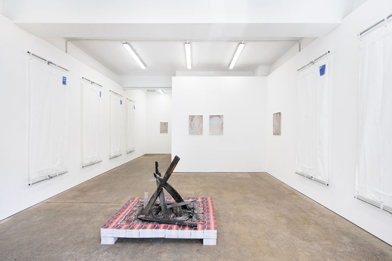 Art gallery with minimalist white walls featuring abstract paintings and a central charred wood sculpture on a platform.