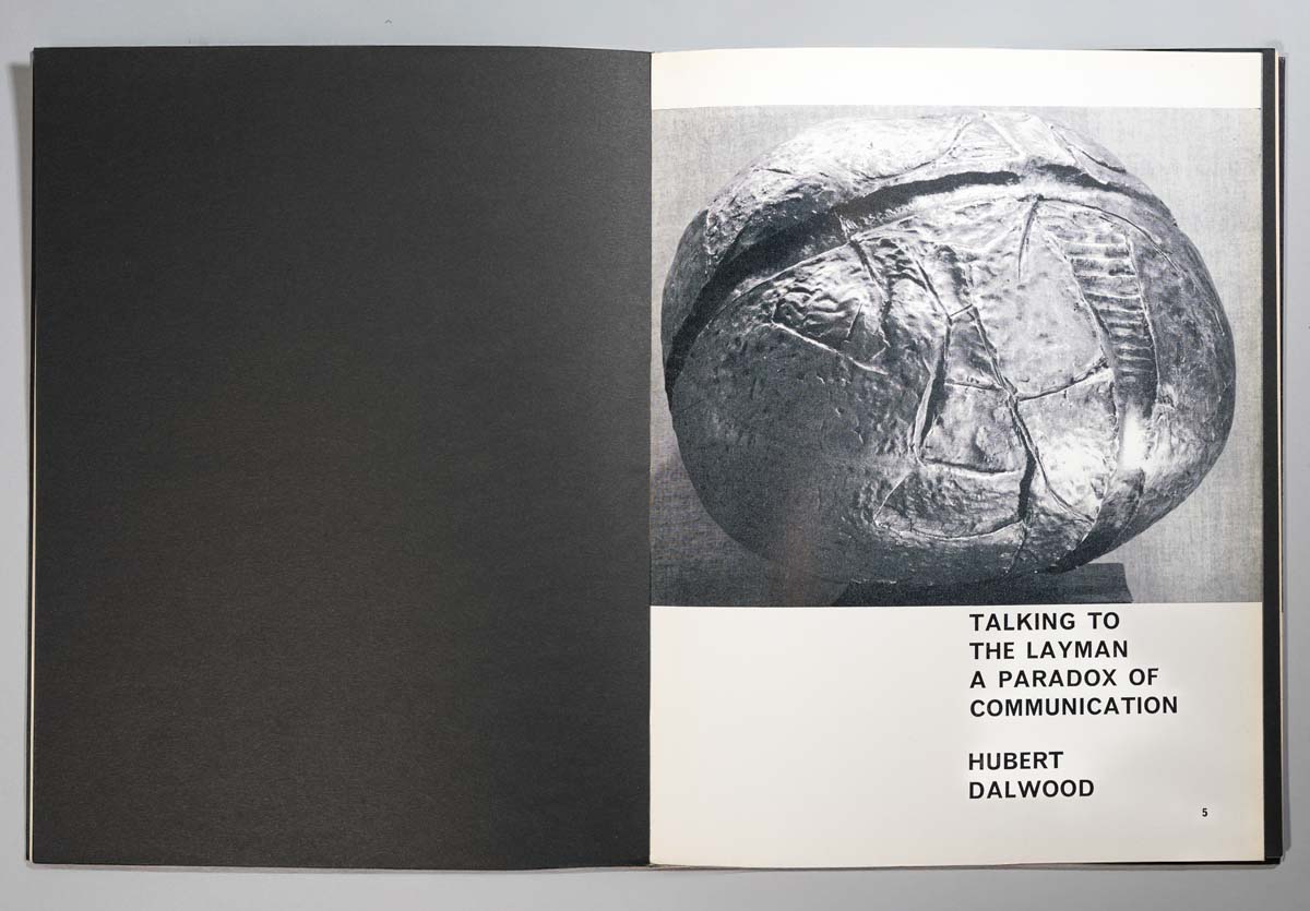A photograph of an open book showing a black and white sculpture photo on the right page, titled "Talking to the Layman: A Paradox of Communication" by Hubert Dalwood.