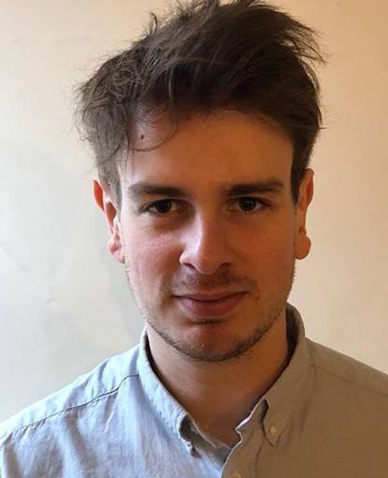 Headshot of artist Thomas Harker wearing a grey collared shirt.