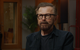 A man with glasses and a beard is sitting in a room.