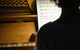 A person sitting by a piano looking at sheet music