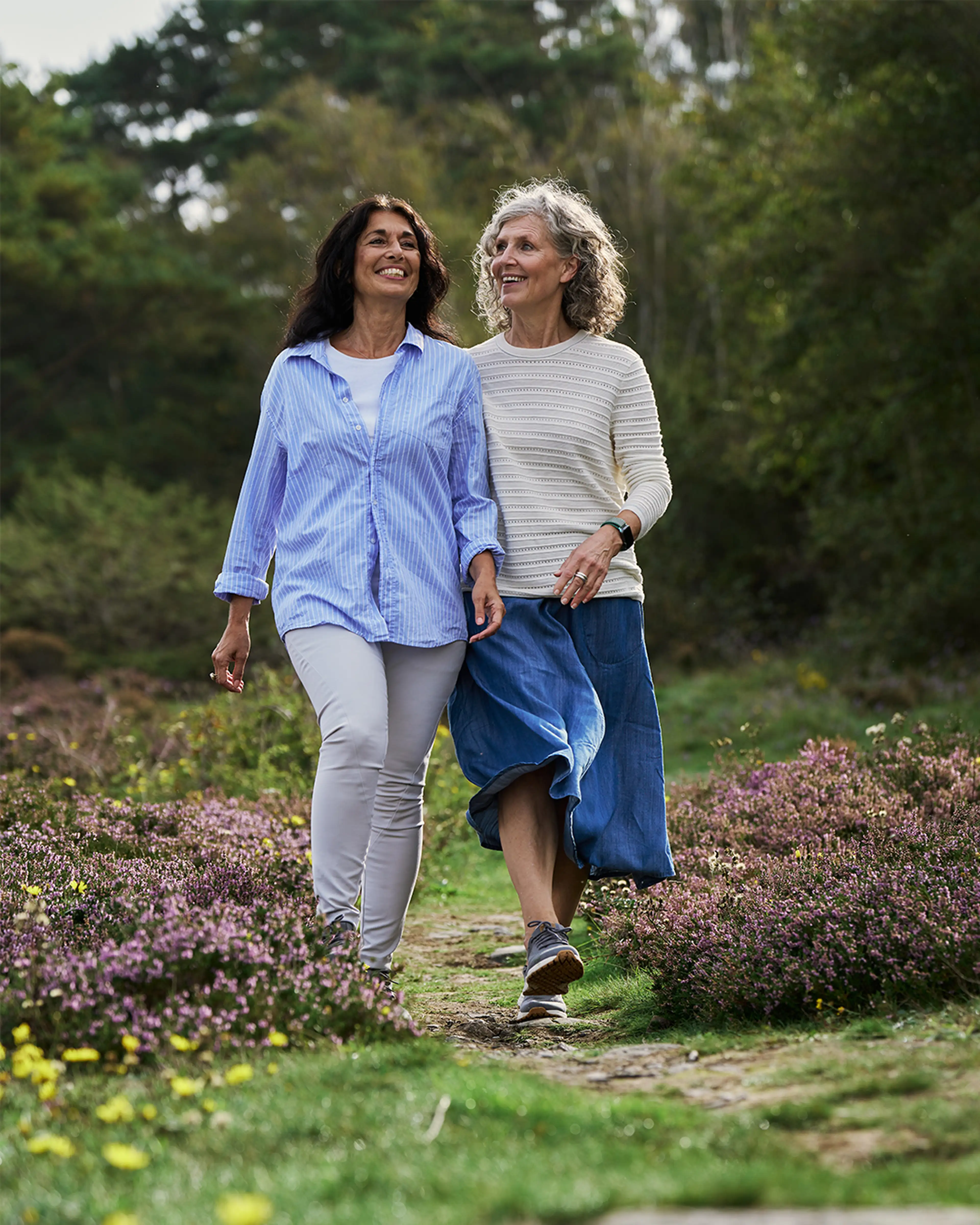 Two women walking down a forest path, smiling and enjoying time in nature.