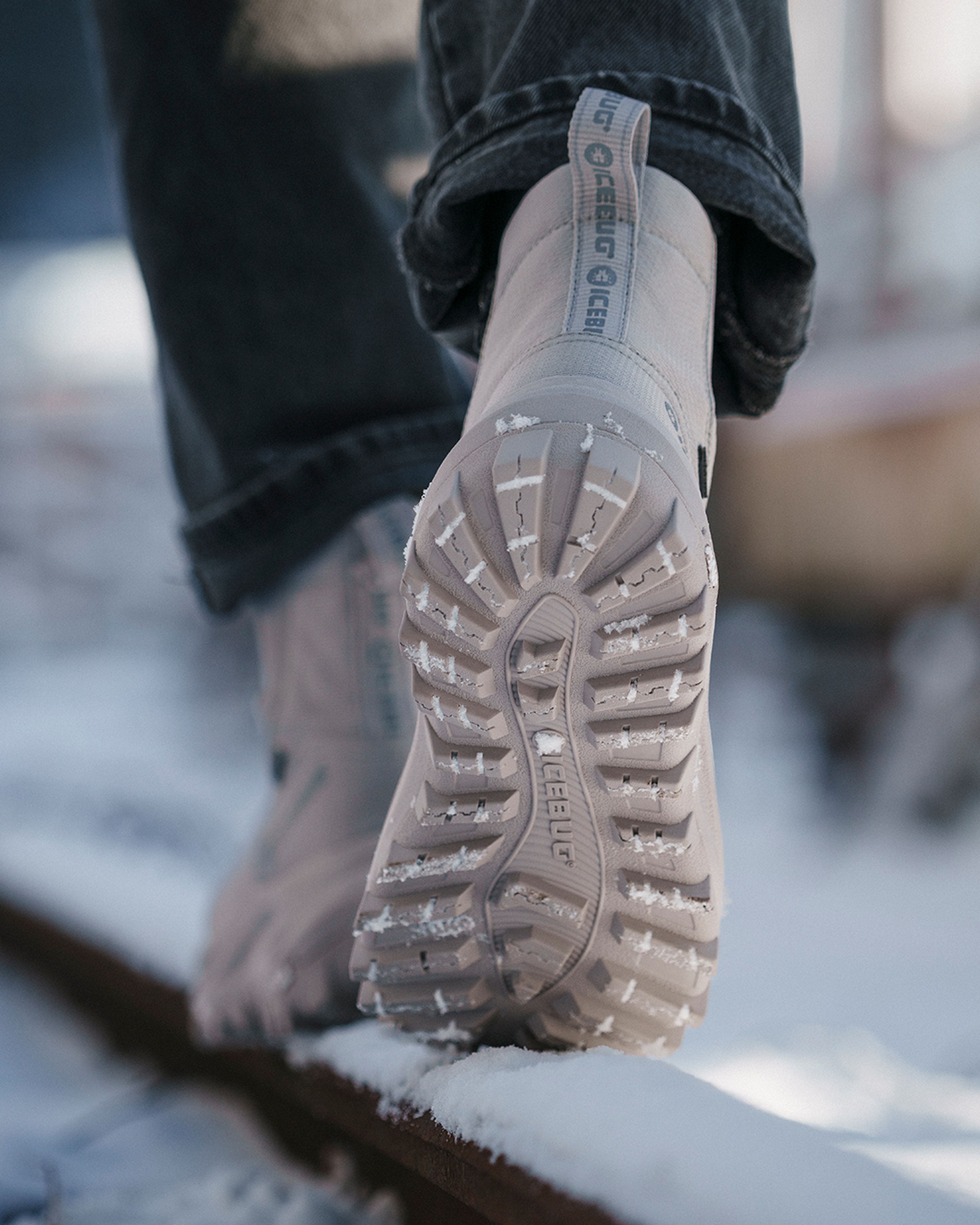 Close-up of a person walking on a snowy surface, wearing beige boots with deep treads.