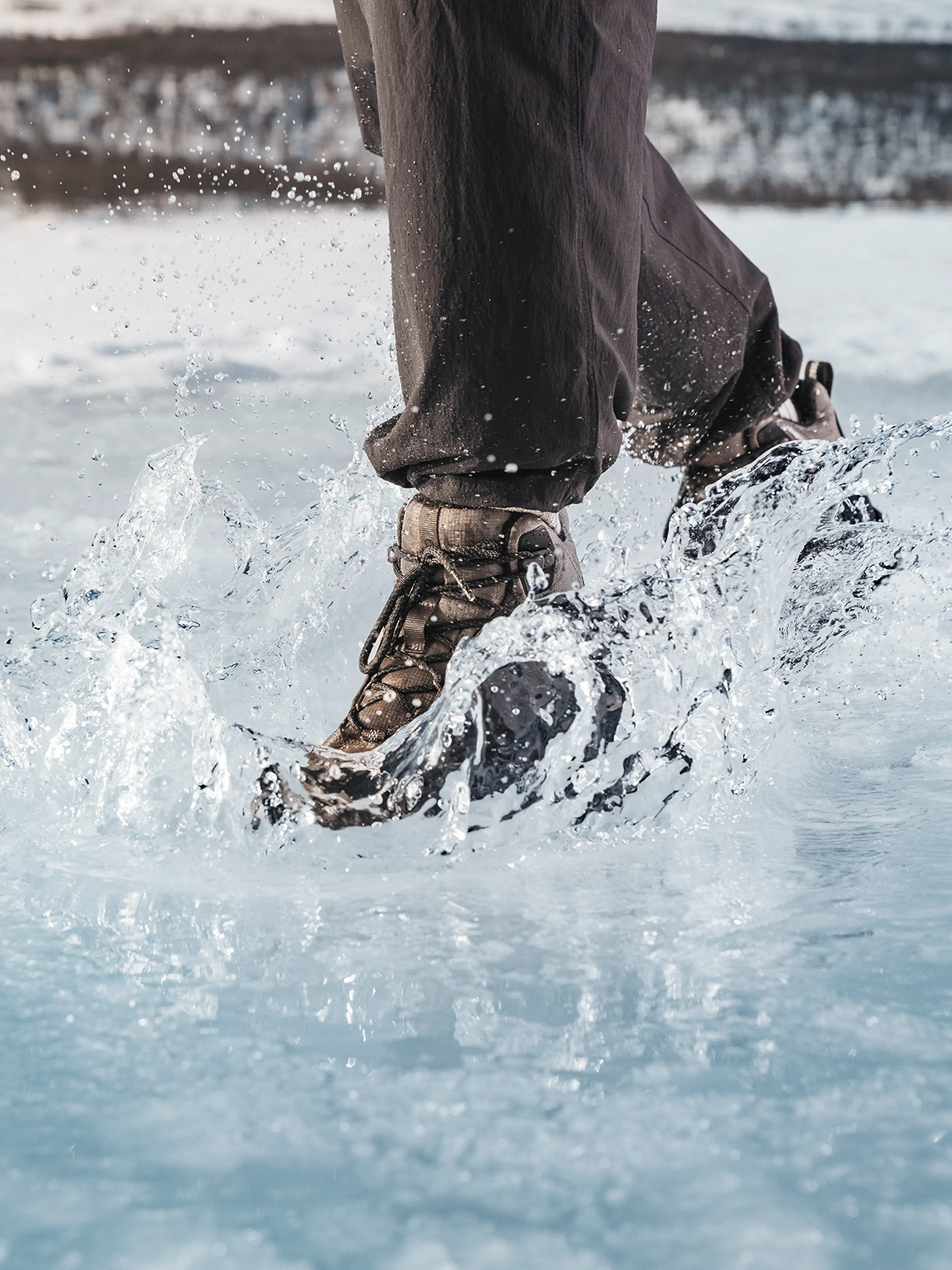 Close-up of a person walking with hiking boots on icy ground, splashing water around.