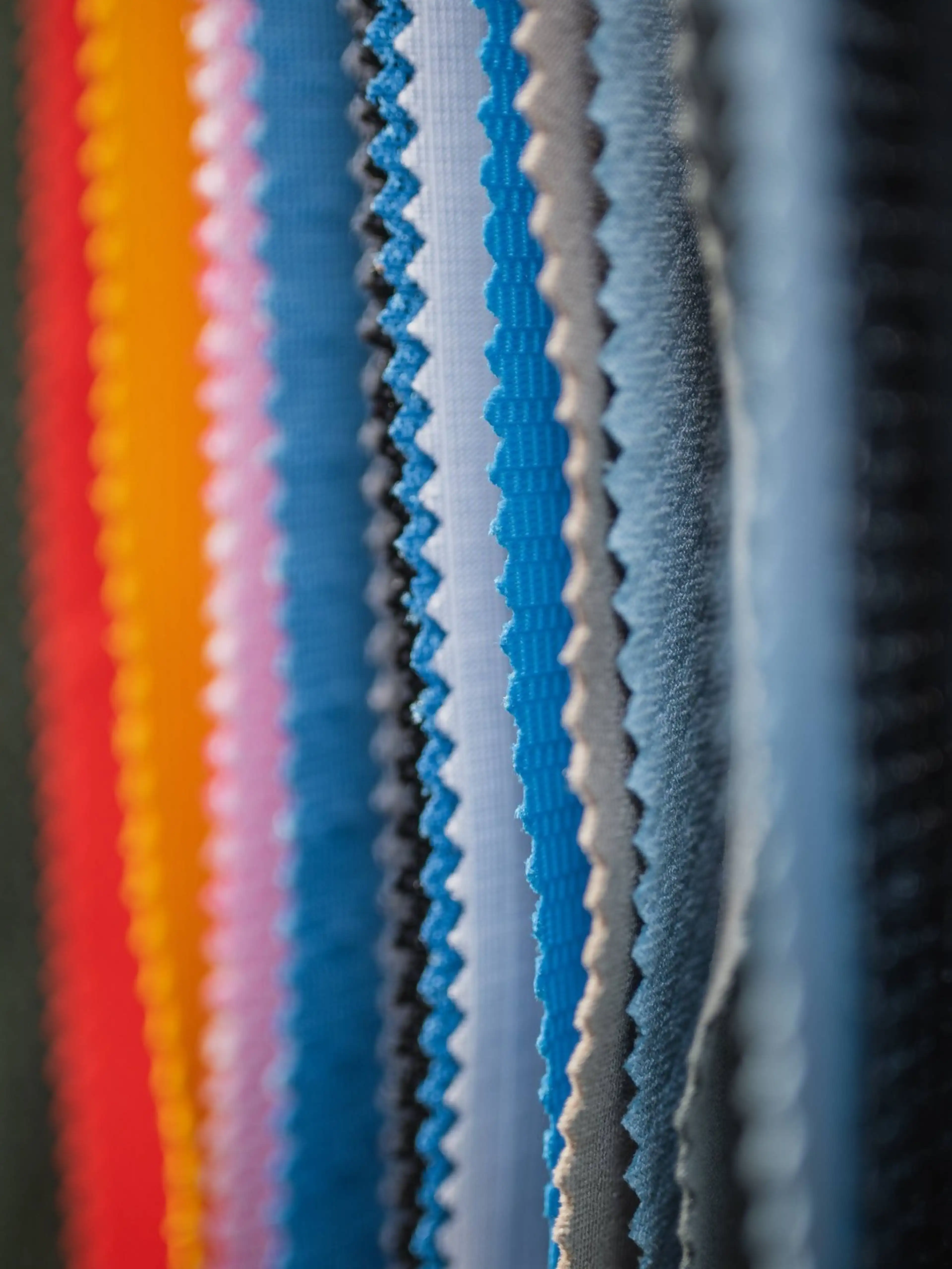 Close-up of colorful fabric swatches with zigzag edges, arranged vertically in a row, showcasing a variety of textures and hues.