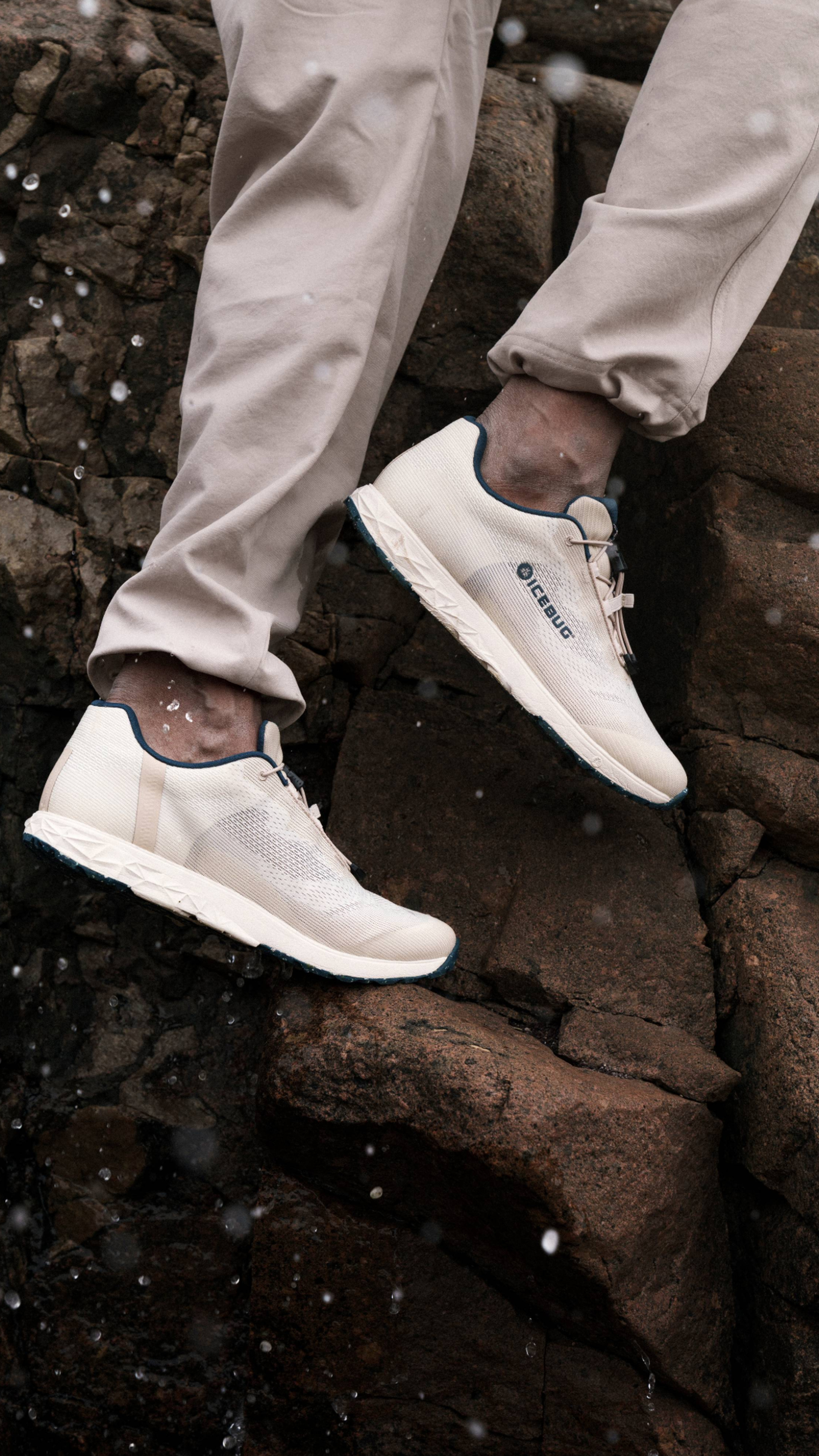 Person wearing white sneakers and light pants stepping on wet rocks with water splashes around.