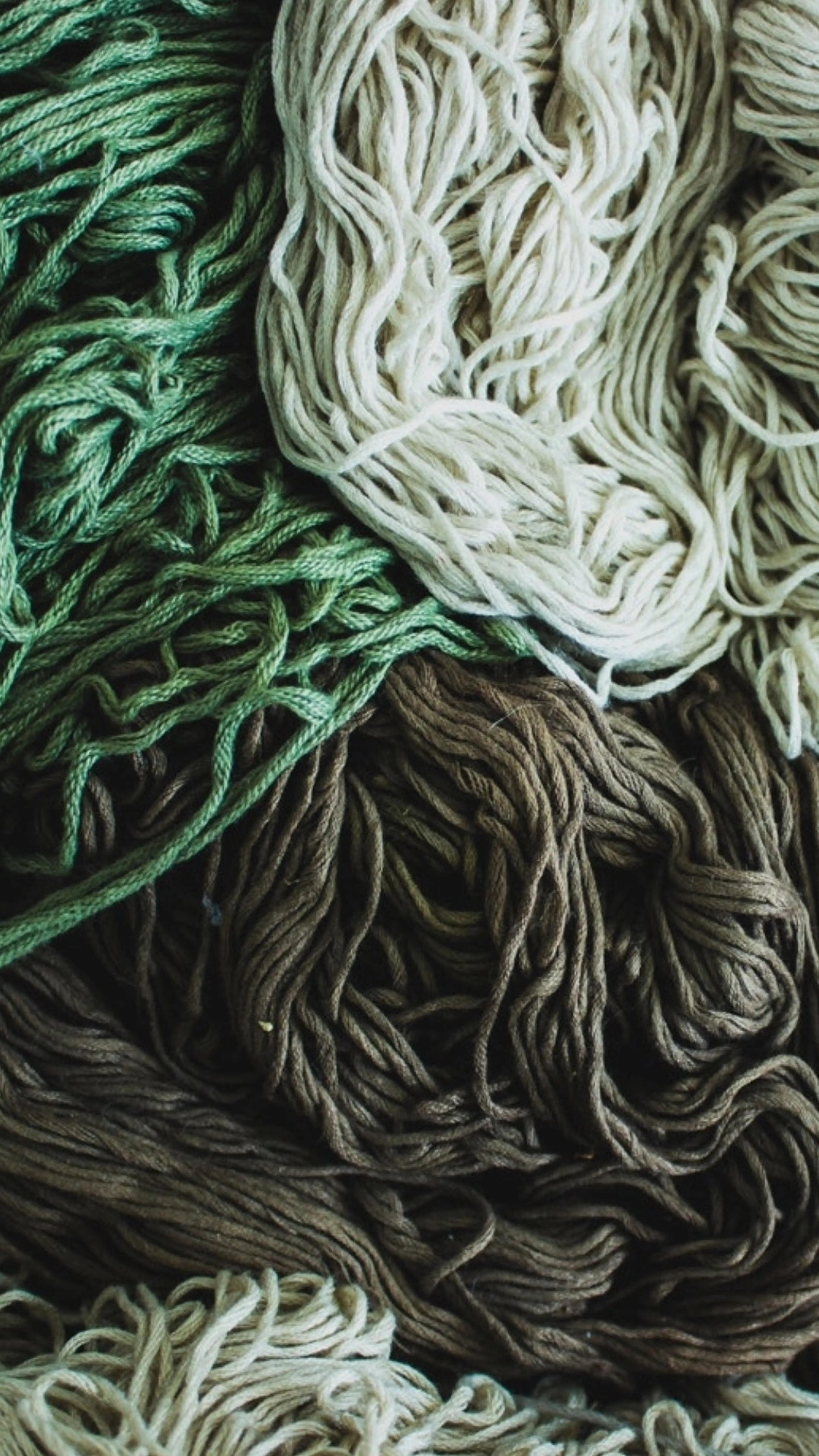 Bundles of yarn in green, cream, and brown shades, intricately tangled together, creating a textured and colorful pattern.