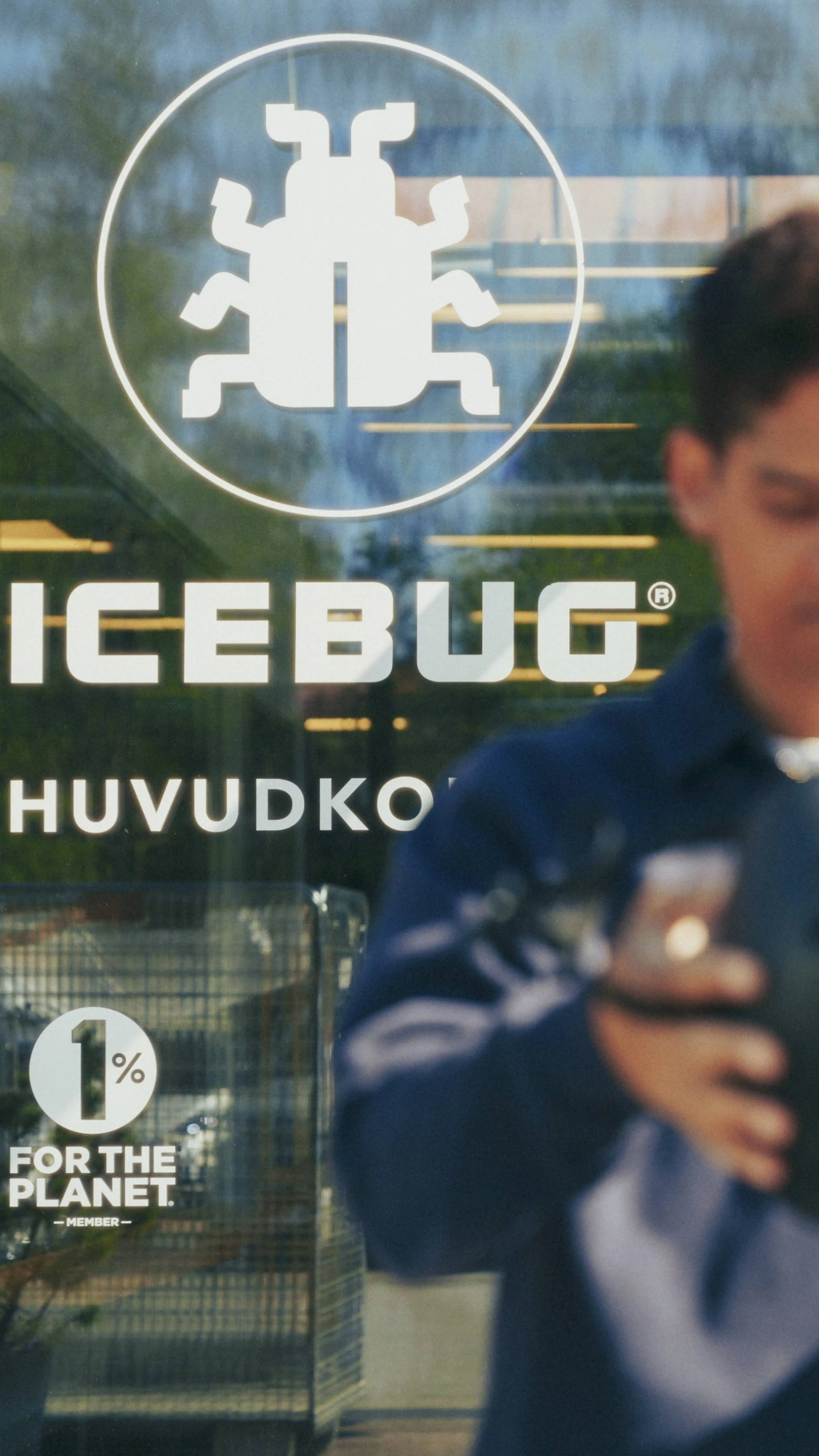 Blurry person in front of a glass door with the Icebug logo and "1% for the Planet" sign in the background.