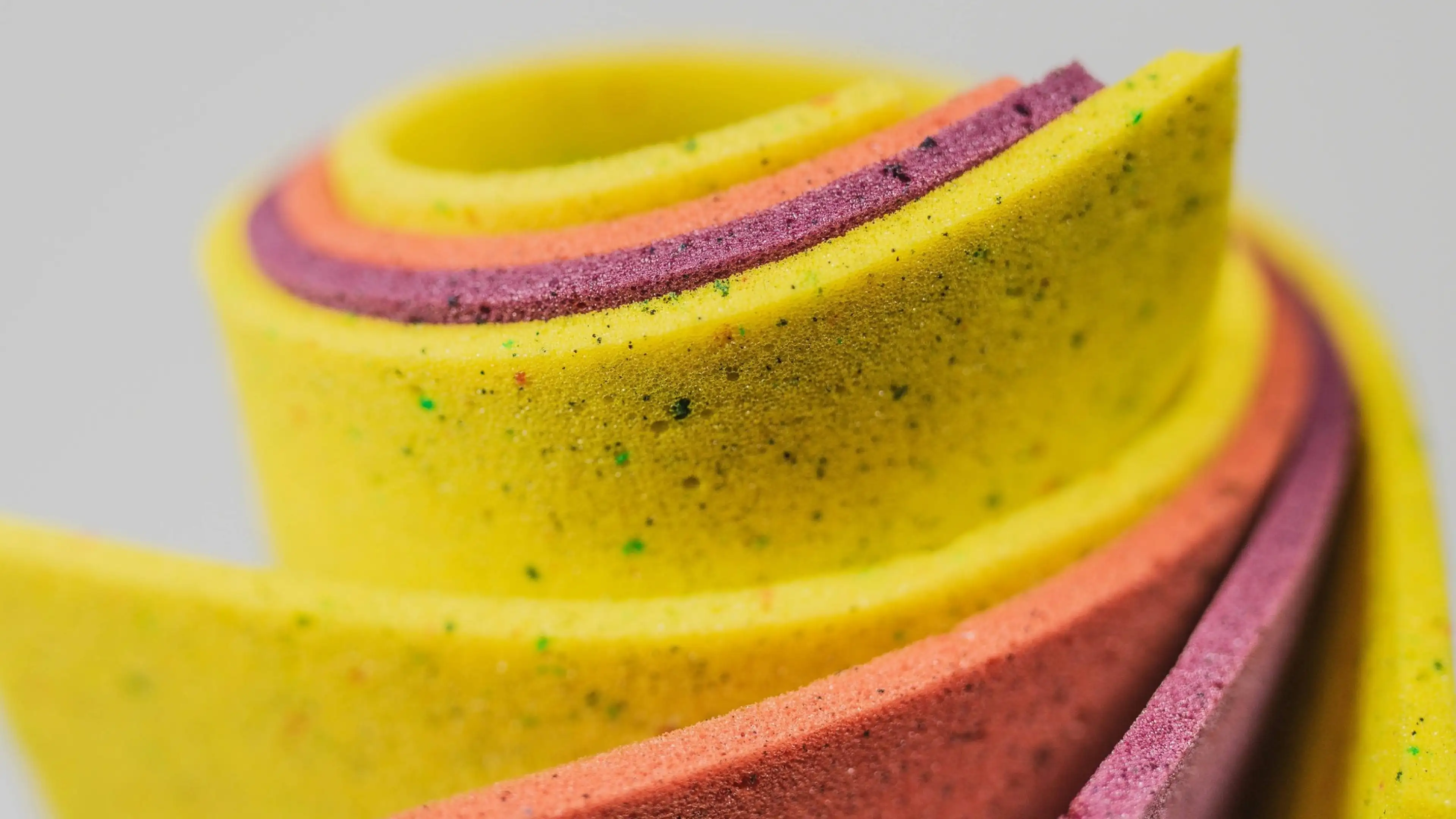 Close-up of a rolled, colorful foam with yellow, pink, and purple layers, displaying a speckled texture.