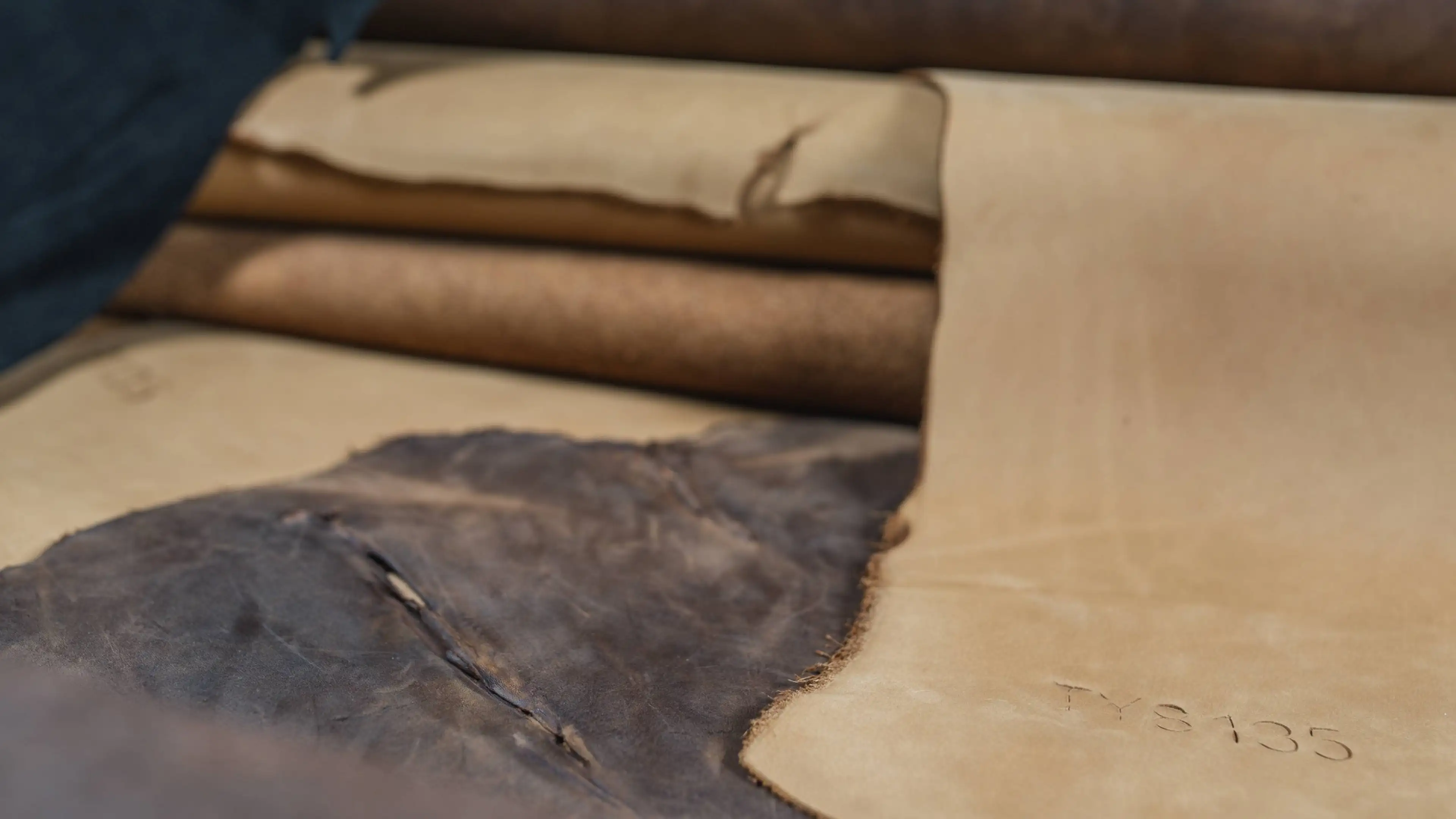 Stacks of rolled leather in beige and brown tones, with visible textures and markings, ready for crafting or production.