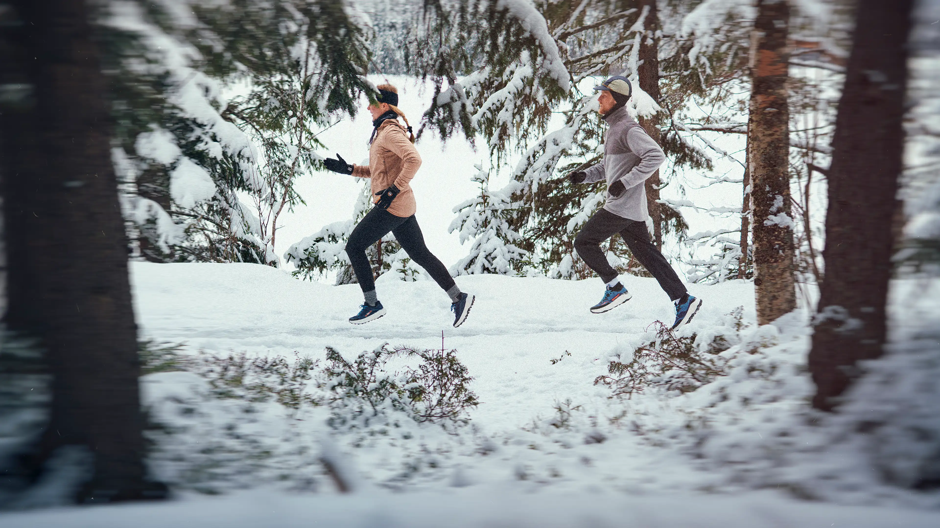 Two people jogging through a snow-covered forest, wearing winter gear, with pine trees in the background and a serene, wintry atmosphere.