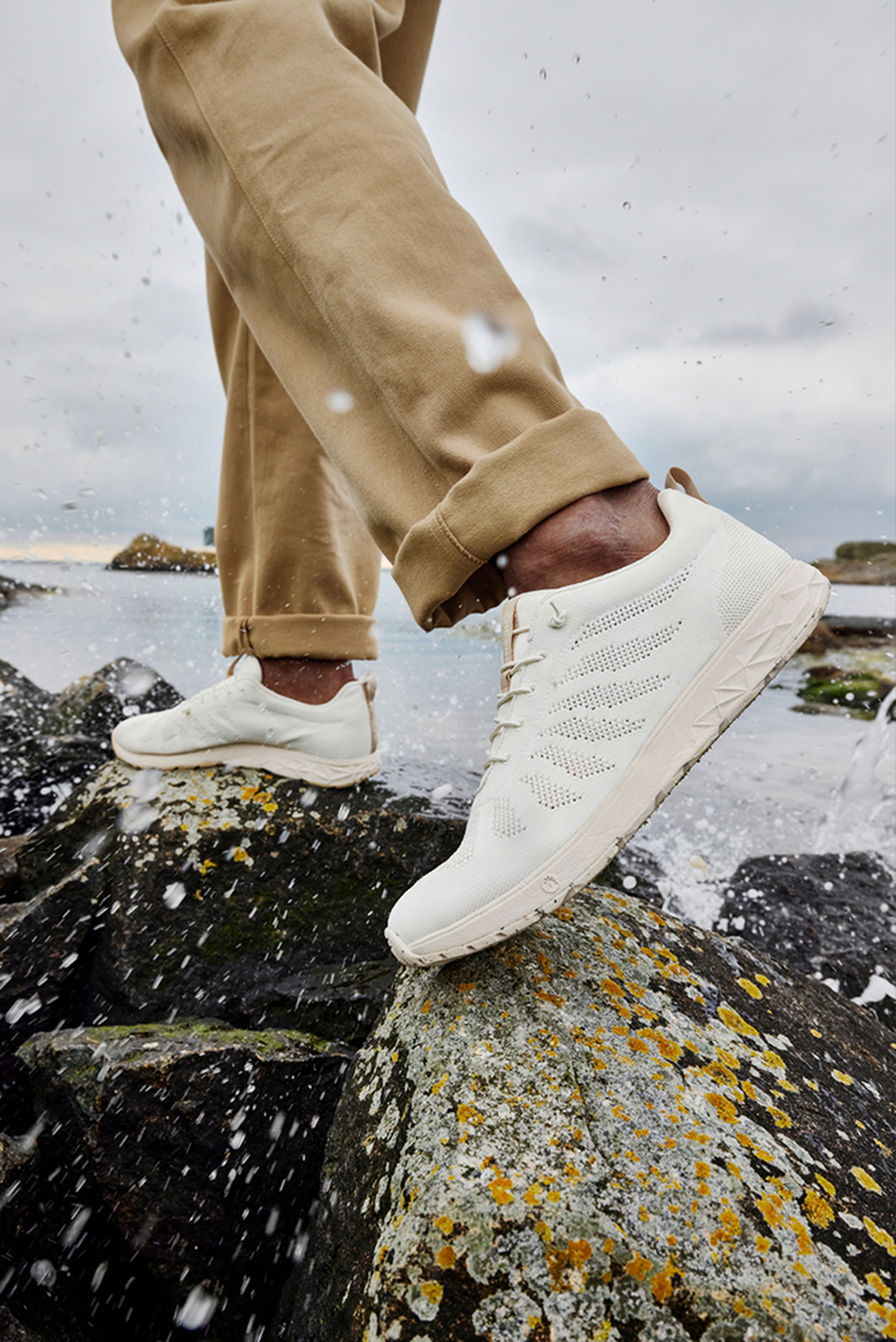 A person walking on rocks by the sea, wearing white sneakers from Icebug.
