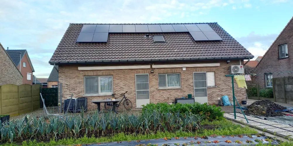 Back of a house with brick facade, PV panels on the roof, and a garden planted with vegetables.