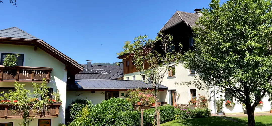 Charming country house with wooden balcony and garden featuring trees, bushes, and many flowers.
