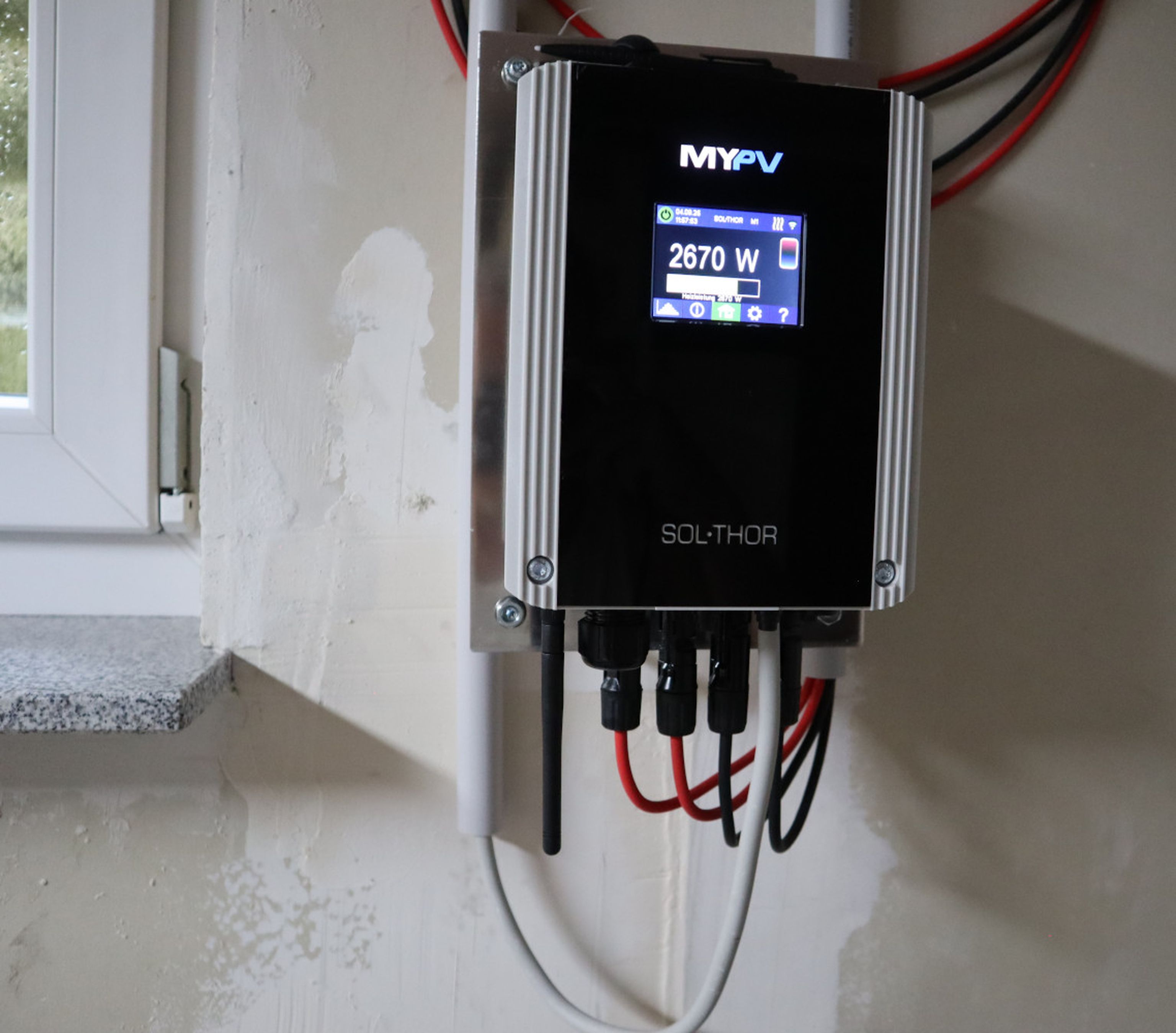 Wall-mounted solar power inverter with a digital display showing "2670 W." Multiple cables are connected below.