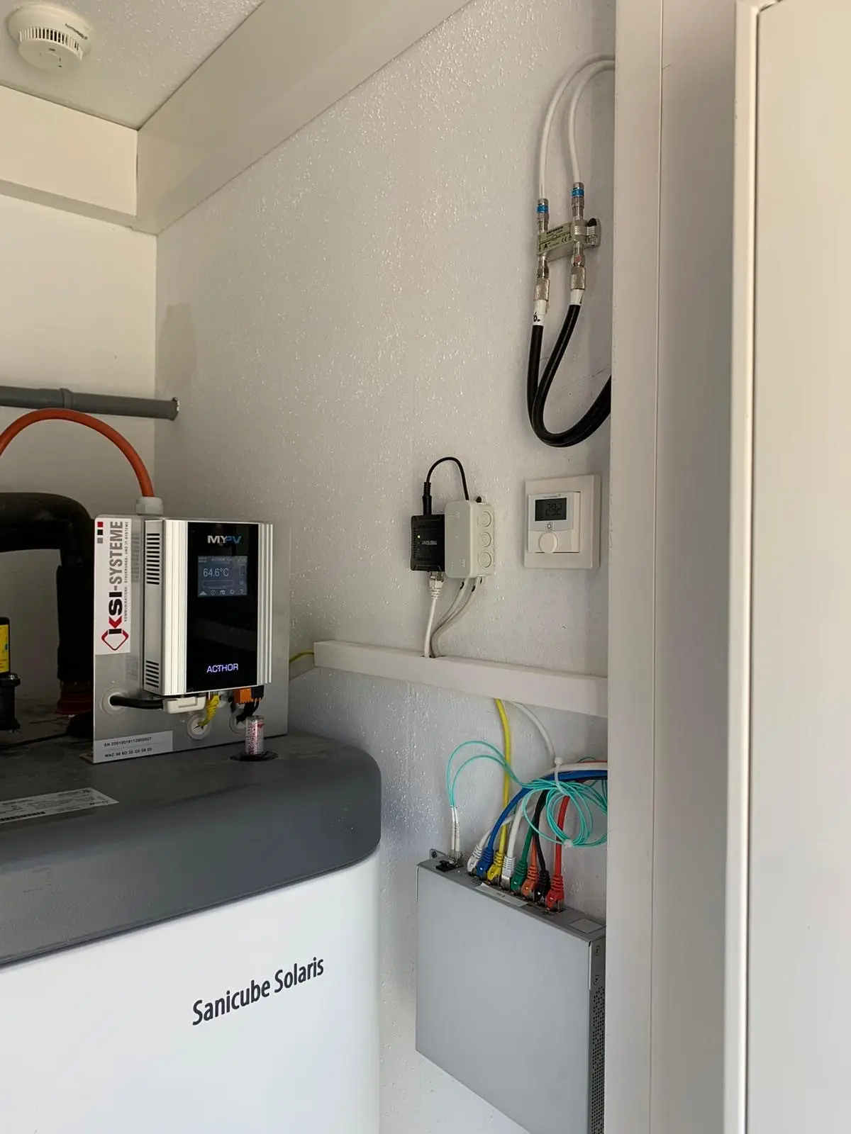 Utility room with Sanicube Solaris system, AC•THOR, and various cables and pipes on the wall.