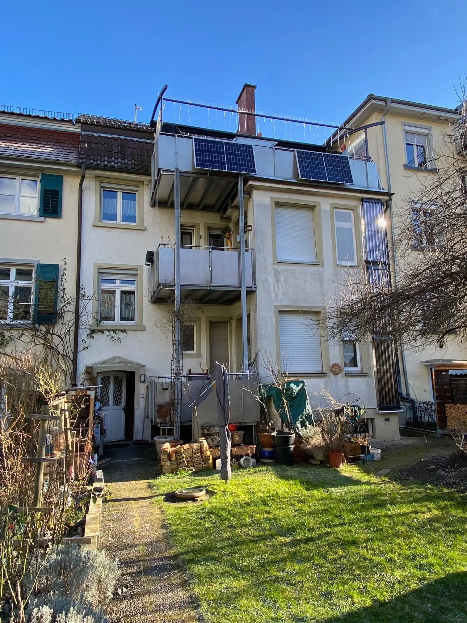 Garden of a renovated old building with a view of balconies equipped with compact balcony PV systems.