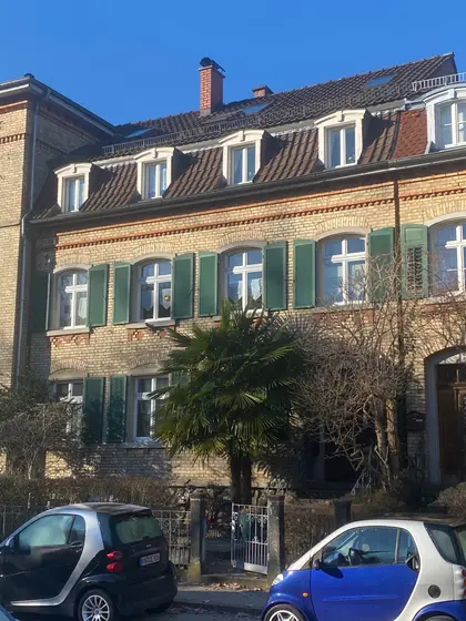 Renovated historic building with green shutters, palm tree in front yard, and two Smart cars parked in sunshine.