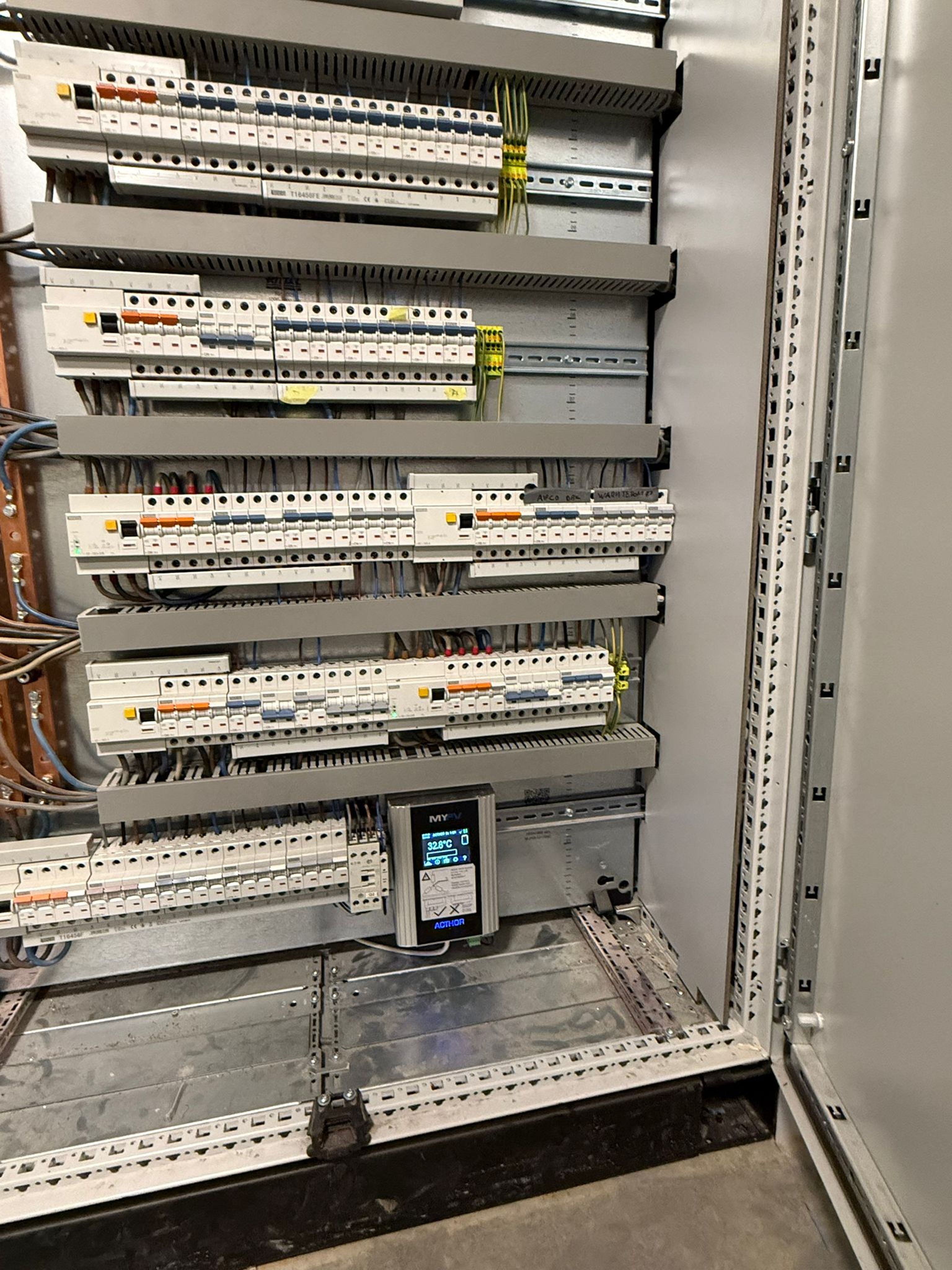 An open electrical panel with multiple rows of circuit breakers and a digital display in a gray metal cabinet.