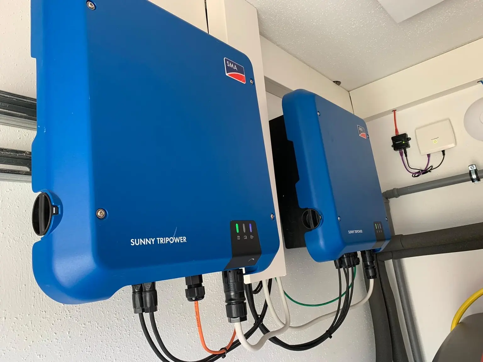 Two blue Sunny Tripower inverters mounted on a wall, with cables connected below, in a clean, well-lit room.