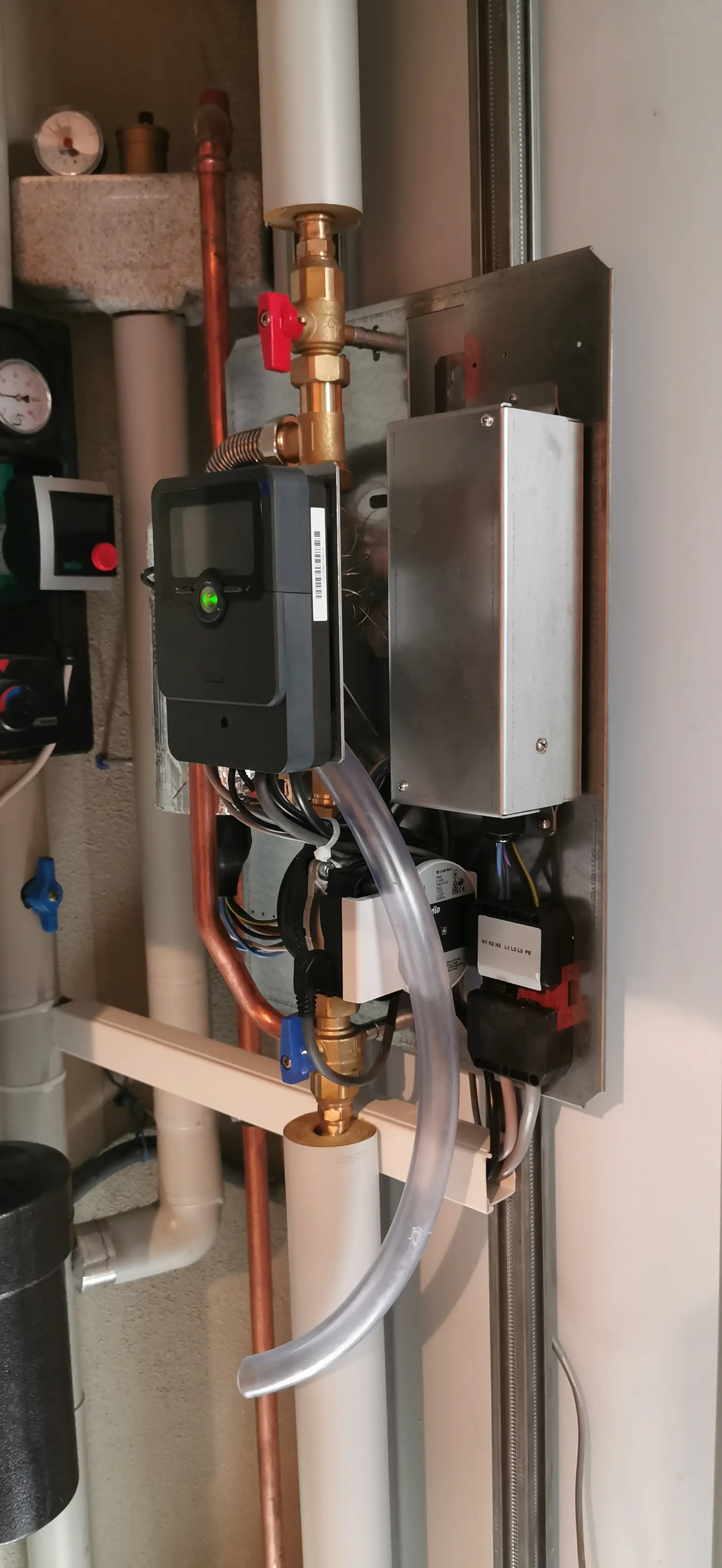 Close-up of mechanical setup with pipes, gauges, and digital control unit with wiring and tubing on metal panel.
