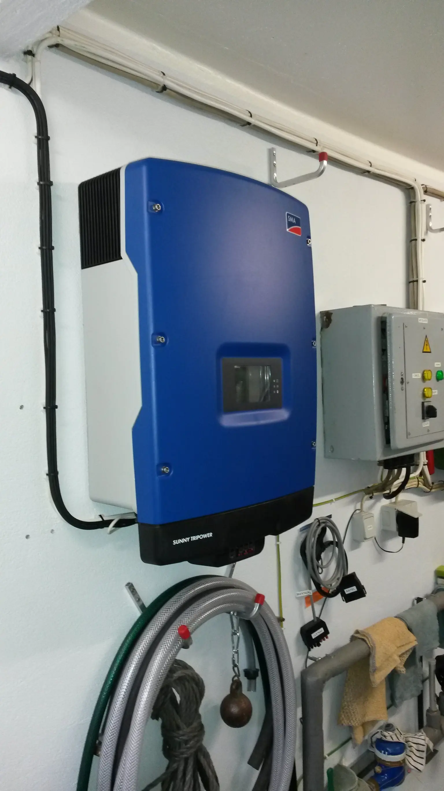 Wall-mounted SMA Sunny Tripower inverter with connected cables, located in a utility room next to a control panel and tools.