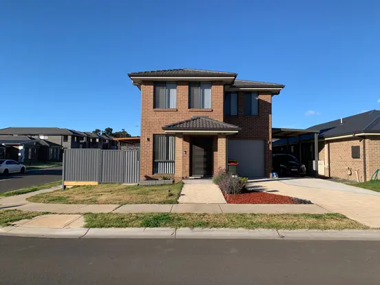 Two-story brick house with small front yard, driveway, and garage under a clear blue sky.