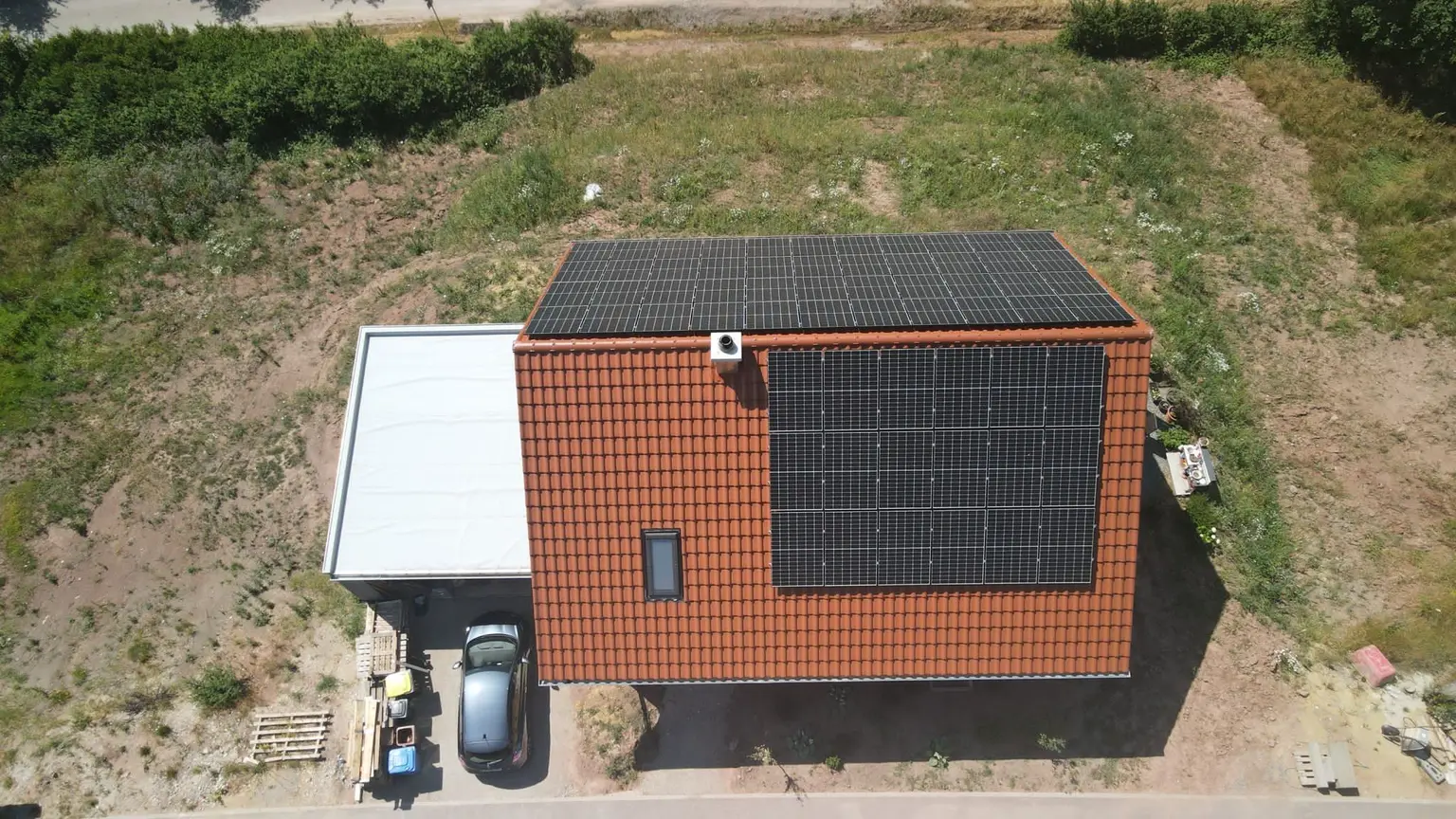 Bird’s-eye view of a house with PV panels and a skylight on the roof, an adjacent garage, and a newly planted garden.