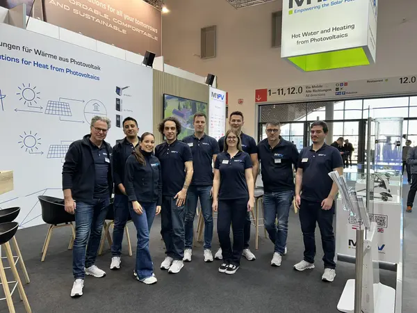 A group of nine people in matching navy shirts pose at a trade show booth with solar energy displays and informational banners.