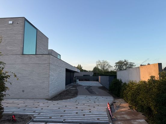 Modern building with large glass windows, minimalist design, and a paved pathway, set against a clear blue sky.