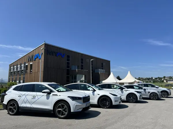 Five white my-PV company cars in front of the building with wooden facade, logo, and solar panels.