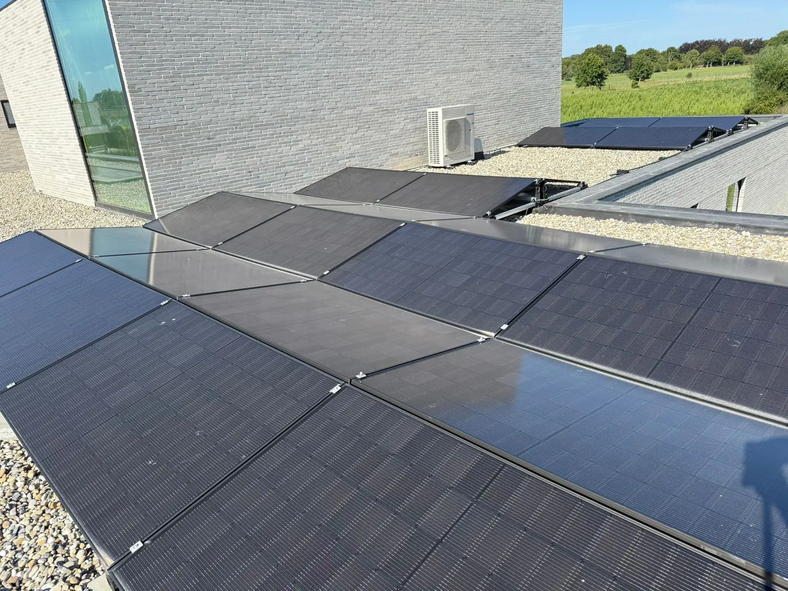 Rooftop solar panels on a modern building with a stone facade, set against a sunny, green landscape.