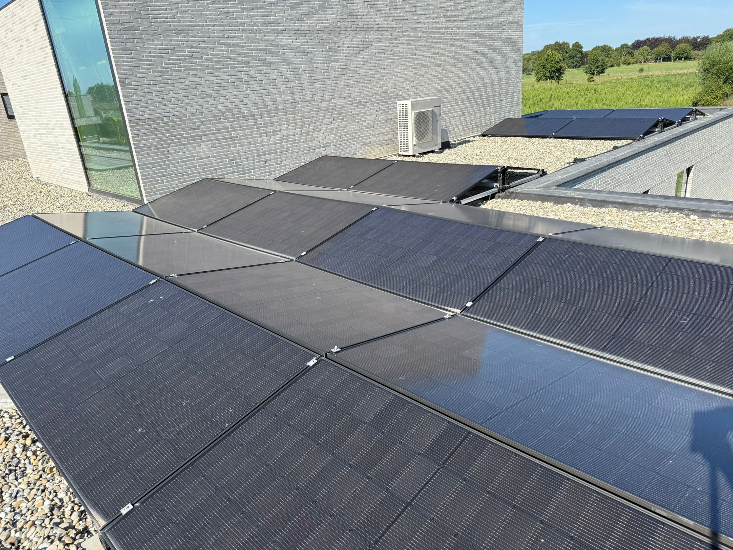 Rooftop solar panels on a modern building with a stone facade, set against a sunny, green landscape.