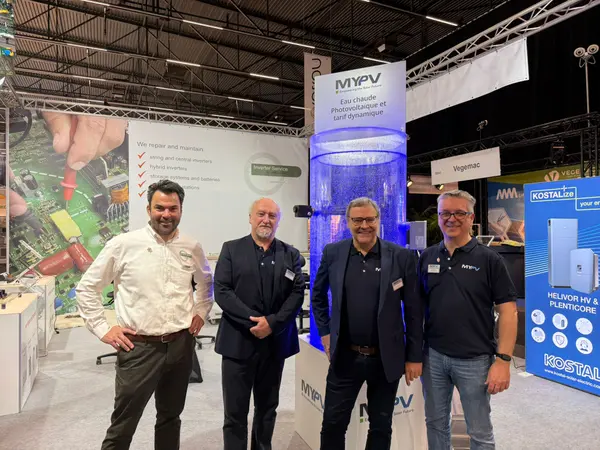 Four men standing together at a technology trade show booth featuring MyPV products, with banners and displays in the background.