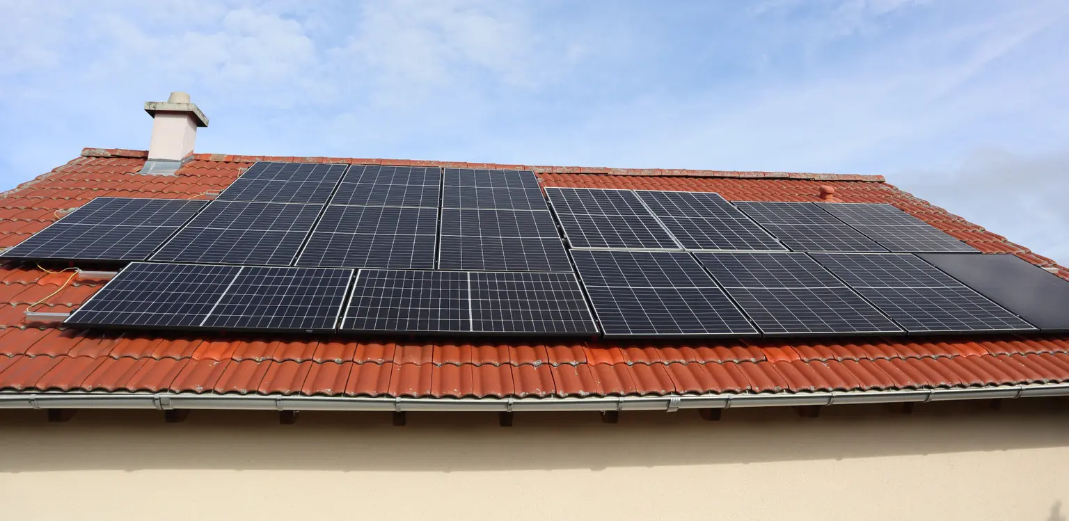 Solar panels installed on a red-tiled roof of a house under a blue sky.