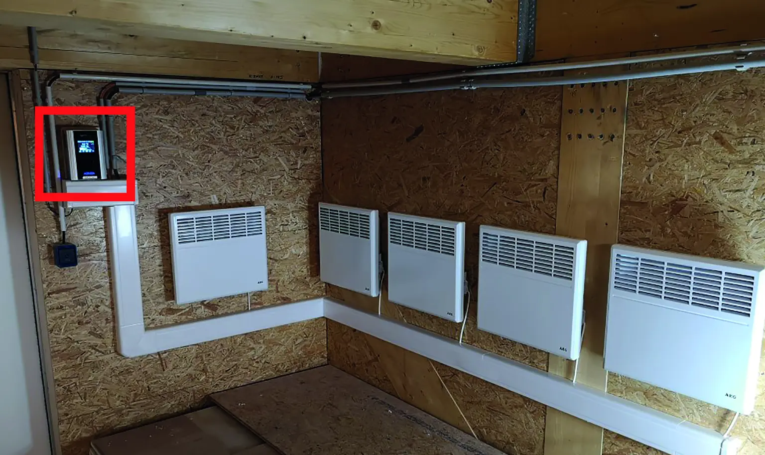 Room with five wall-mounted heaters, a mounted AC•THOR, and visible electrical wiring on a wooden wall.