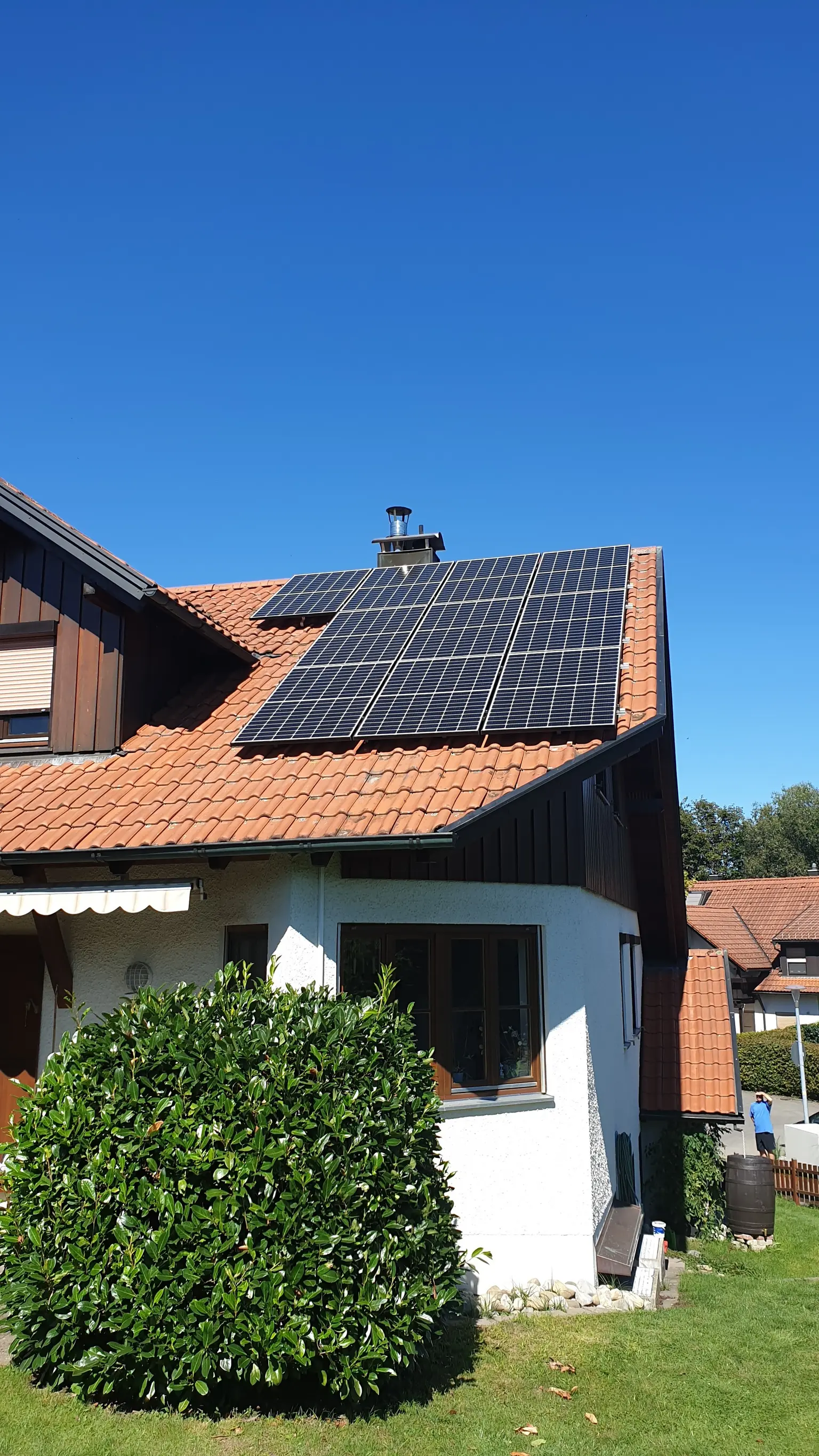 House with white facade and wooden windows, seen from garden in summer, with PV panels on the roof.