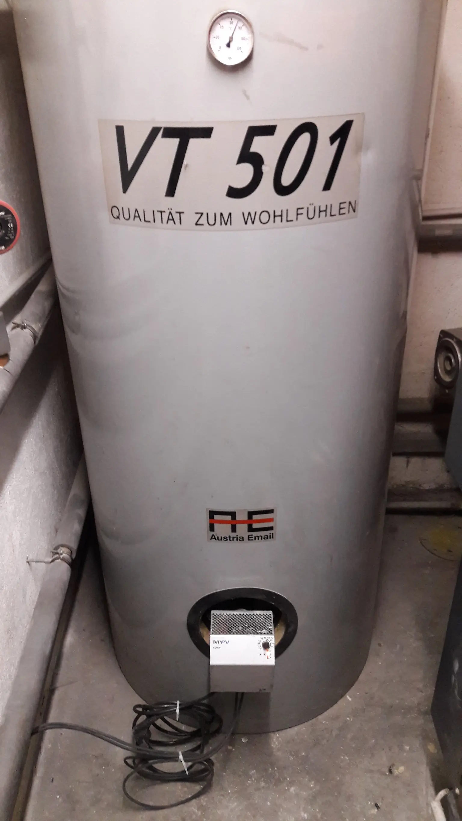 Large gray water heater with mounted ELWA and pressure gauge in a utility room.