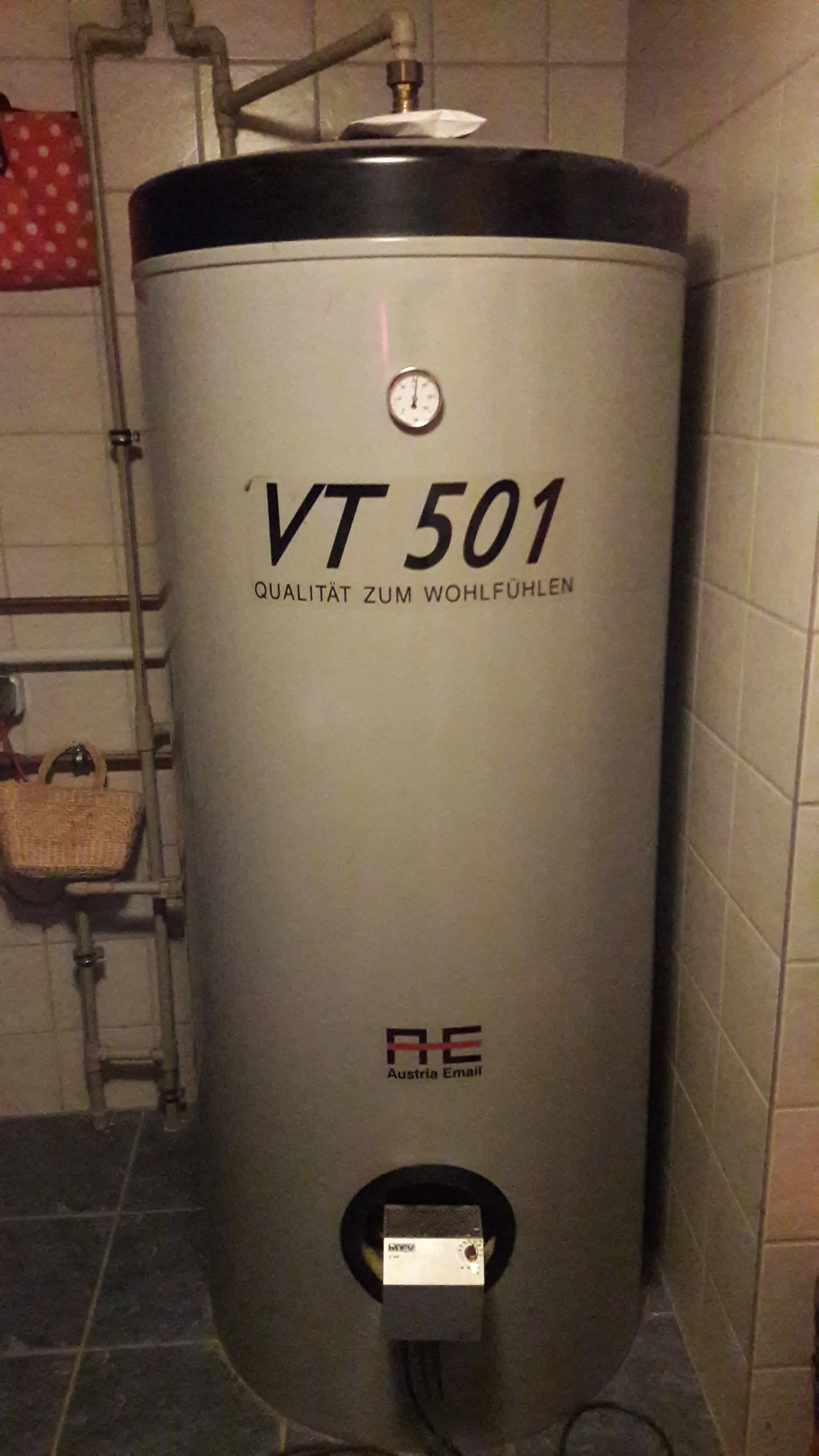 Large gray water heater with mounted ELWA and pressure gauge in a utility room.