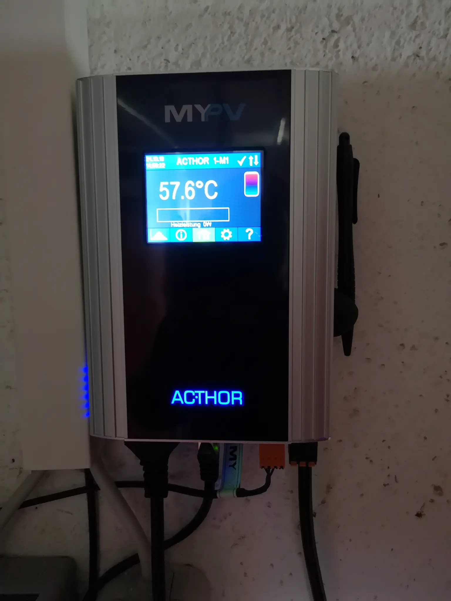 AC•THOR showing 57.6°C, wall-mounted with connected cables and blue-lit 'ACTHOR' label.