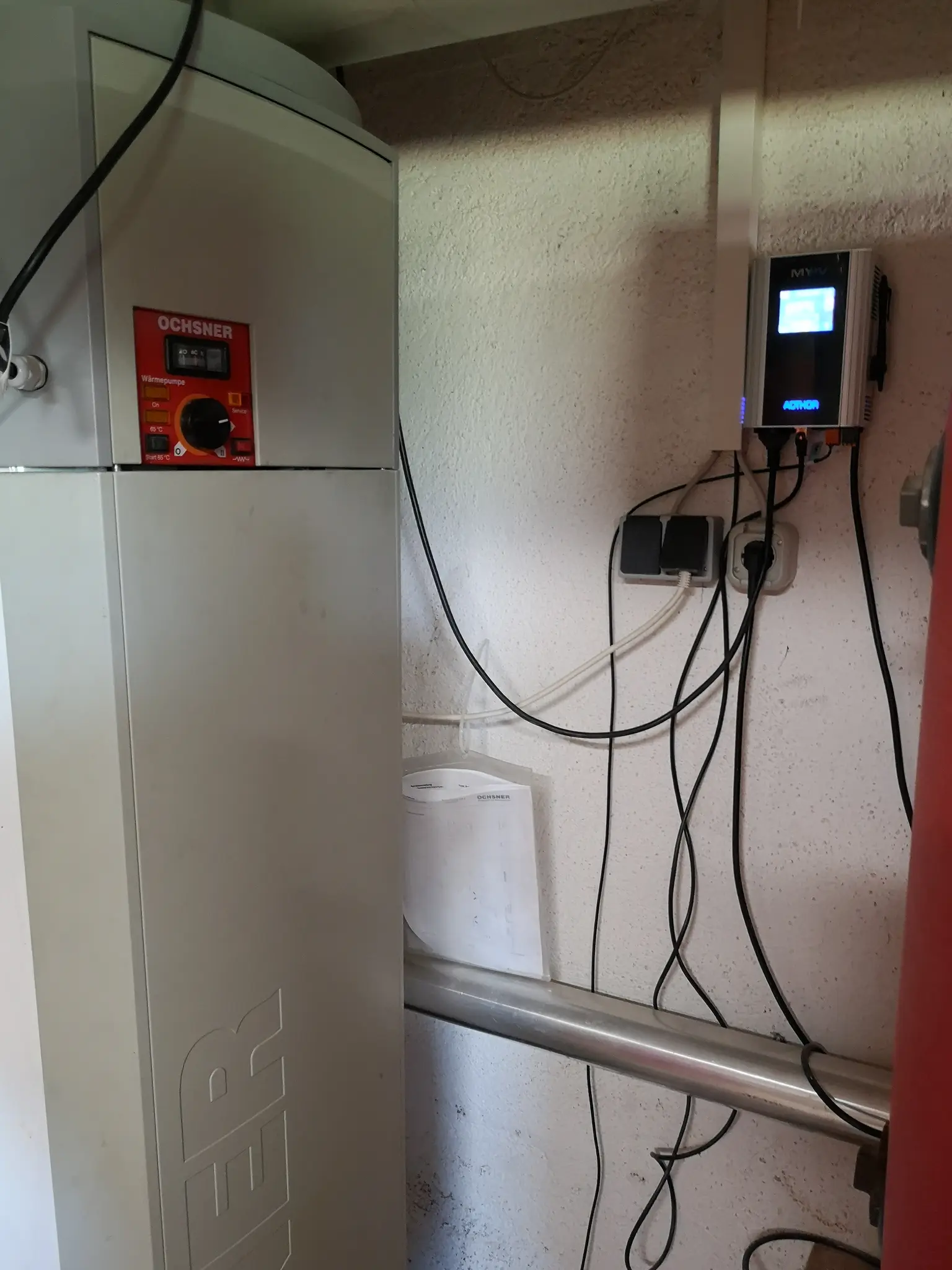 White heating system unit with AC•THOR installed against a wall, connected with various cables and pipes.