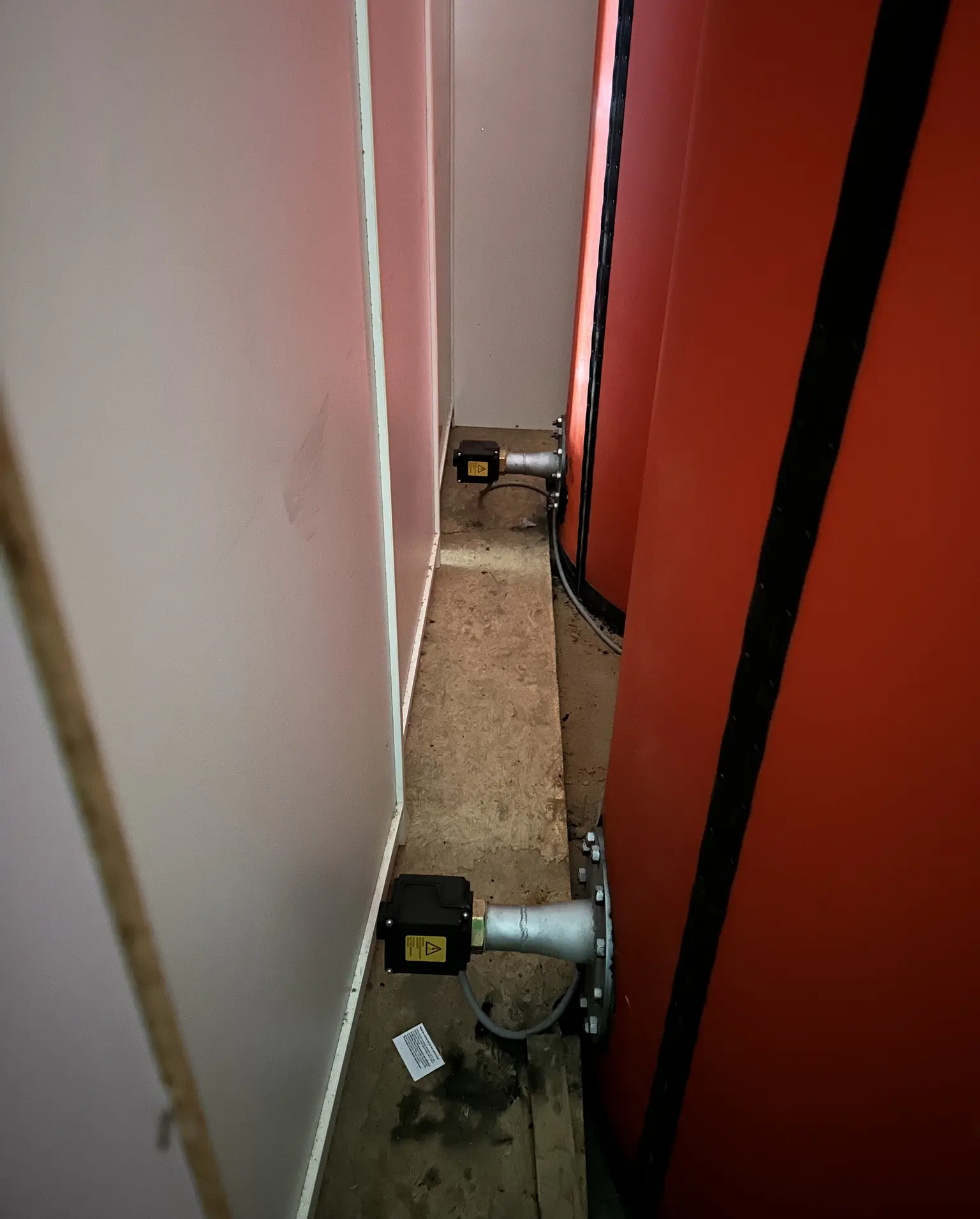 Narrow space with red cylindrical structures, two black sensors on the floor, and a wooden plank in between.