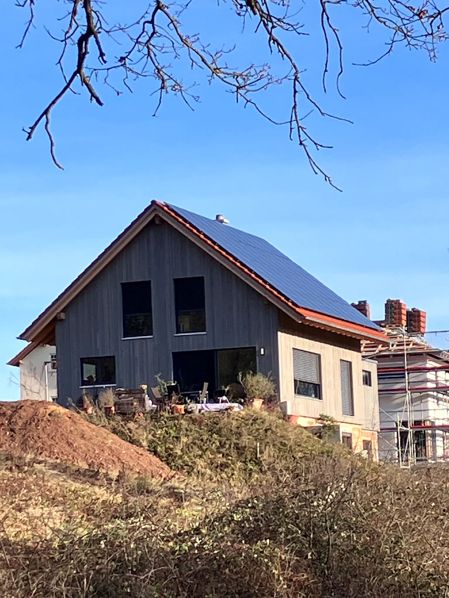 Modern single-family house with wood facade and PV panels on the roof, surrounded by ongoing construction work.